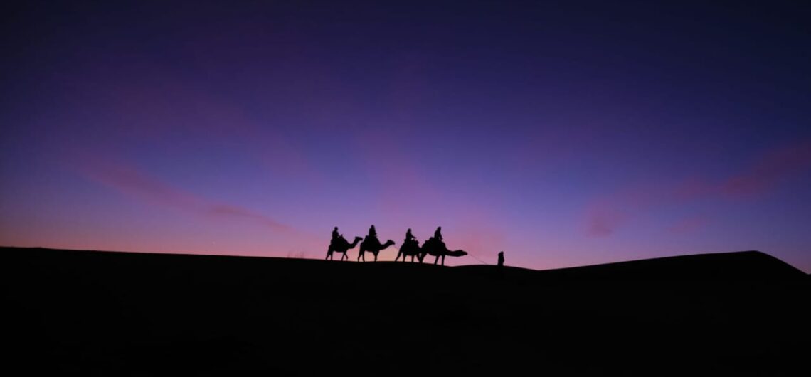 A picturesque scene of a camel caravan making its way back to camp in Merzouga, Morocco, against the backdrop of a stunning desert sunset. Silhouetted camels traverse the sandy dunes, creating a sense of tranquility and adventure. #Merzouga #CamelCaravan #DesertSunset #Travel